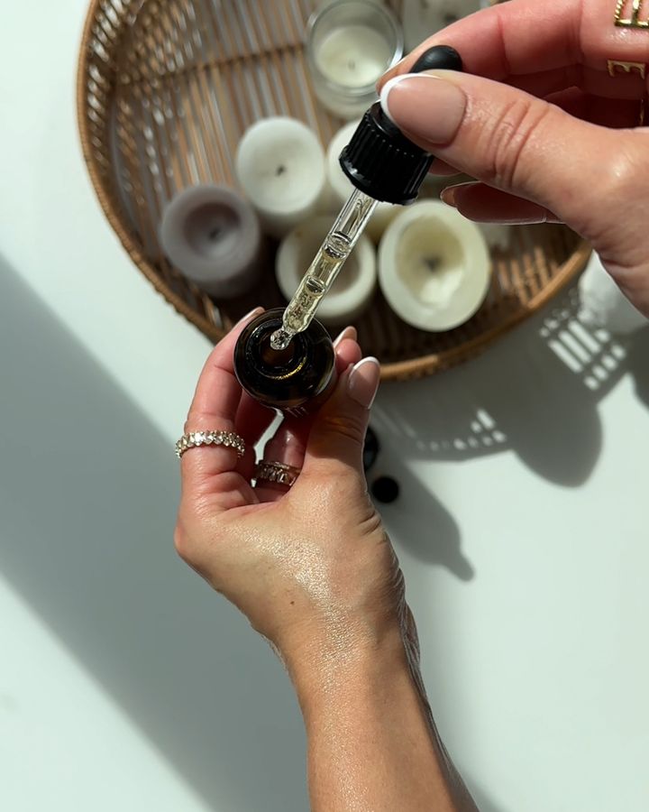 Hände mit Pipette über einem Serum-Fläschchen, Rattan-Tablett mit Kerzen