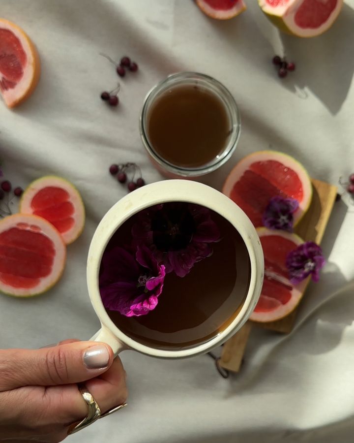 Tasse Tee mit Blüten, umgeben von Grapefruit-Scheiben
