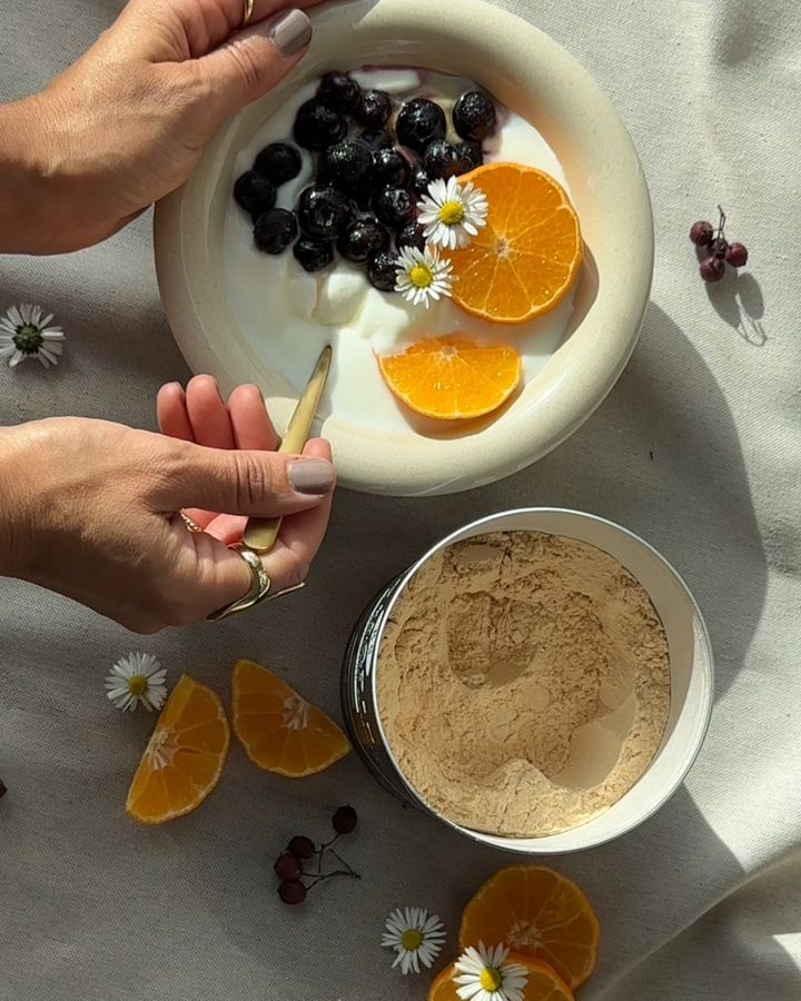 Joghurt-Schale mit Blaubeeren und Mandarinen neben einer Dose Proteinpulver